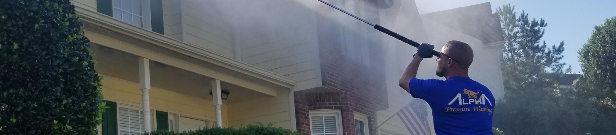 Crew member standing in front of an Alpha Pressure Washing truck beside a house with horizontal siding (2018)
