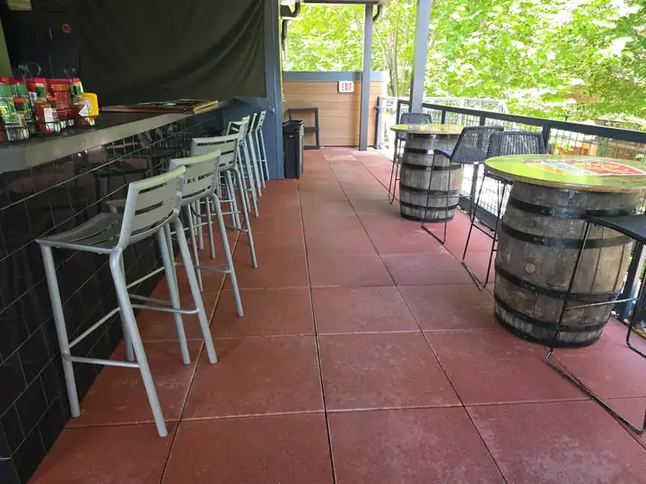 Red-tinted concrete tile floor on a covered rooftop bar patio with barrel tables at a commercial degreasing job in Alpharetta, GA.