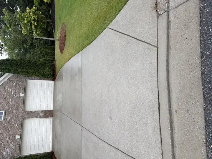 Wide concrete driveway pressure-washed clean in Cumming, GA, brick home with two-car garage and green landscaping