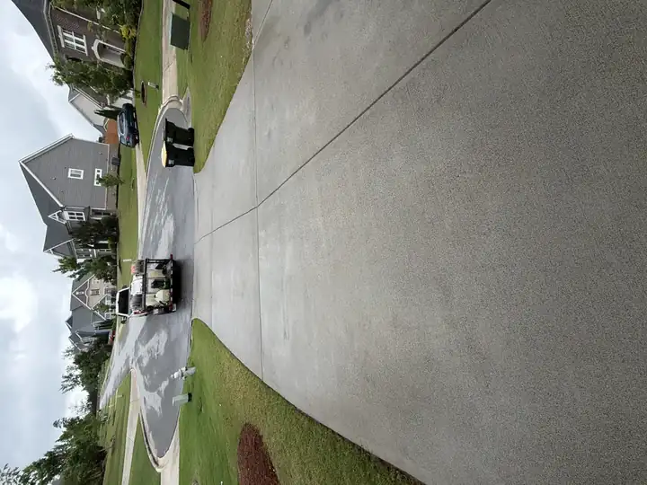 Clean concrete driveway after pressure washing in Cumming, GA, pressure-washing truck visible departing in background