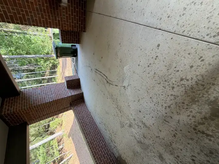 Dirty concrete patio floor under a covered brick pavilion before pressure washing in Alpharetta, GA, showing widespread staining and grime