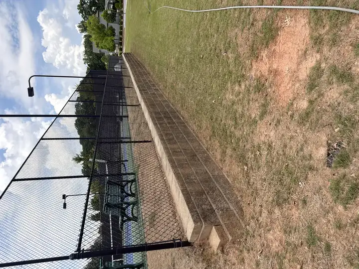 Stone retaining wall and black chain-link pool fence after pressure washing at a commercial pool area in Canton, GA, debris-free and clean