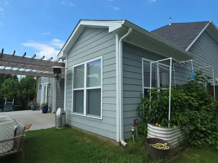 Rear corner of a gray vinyl-sided home with white gutters and a raised garden tub at a house washing job in Canton, GA.