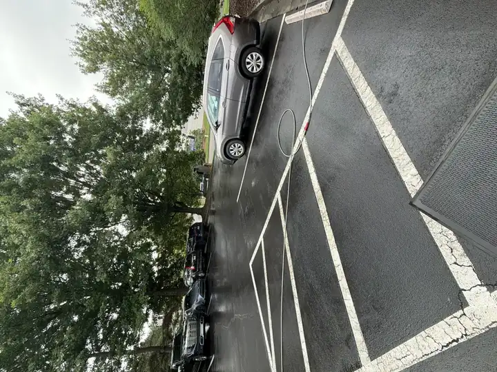 Asphalt parking lot being pressure washed in Alpharetta, GA, with pressure hose laid across wet pavement and parking stall lines visible