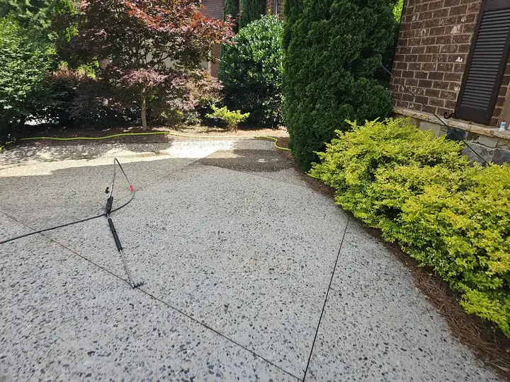 Surface cleaner tool on an exposed aggregate concrete driveway with pressure washing hose in Marietta, GA.