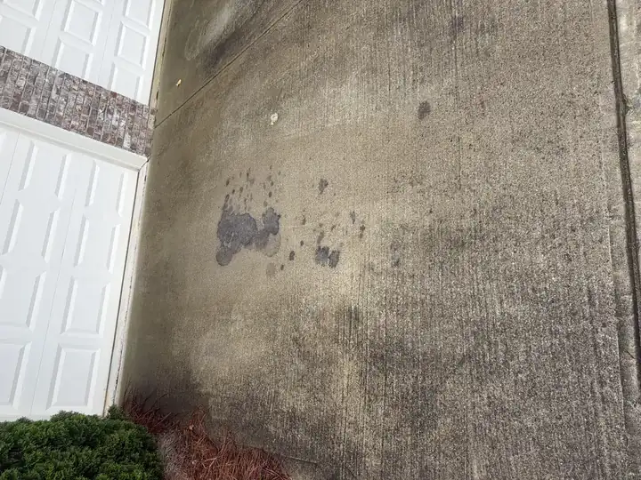Concrete driveway with prominent oil stains near garage before pressure washing service in Cumming, GA
