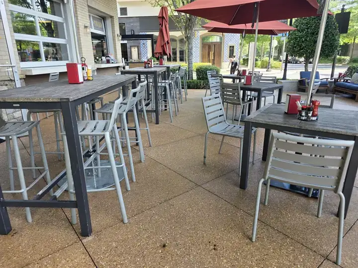 Exposed-aggregate concrete patio with dining tables and red umbrellas at a commercial degreasing job in Alpharetta, GA.