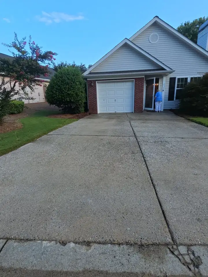 Concrete driveway leading to a brick and vinyl garage at a residential home in Woodstock, GA, with dark staining and grime visible.