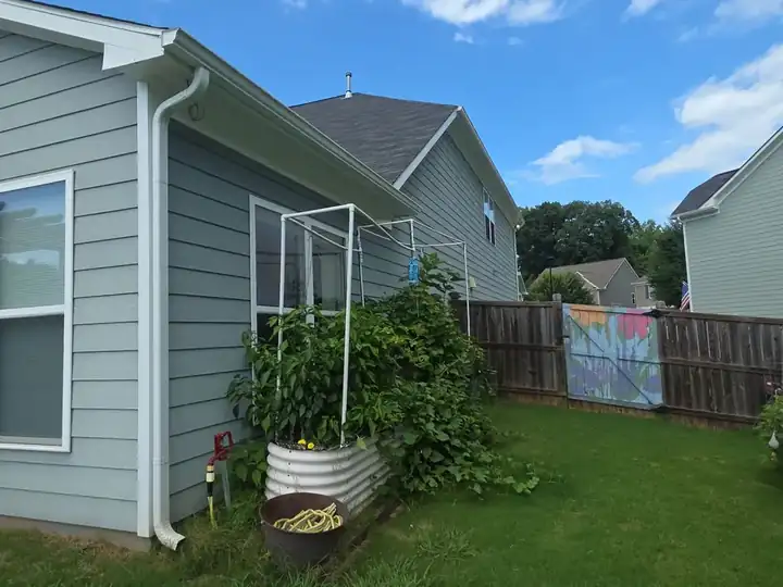 Side of a gray vinyl-sided home with gutters, raised garden bed, and wood fence at a house washing job in Canton, GA.