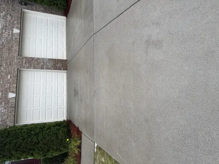 Freshly pressure-washed concrete driveway in Cumming, GA with two-car garage and brick facade visible in background