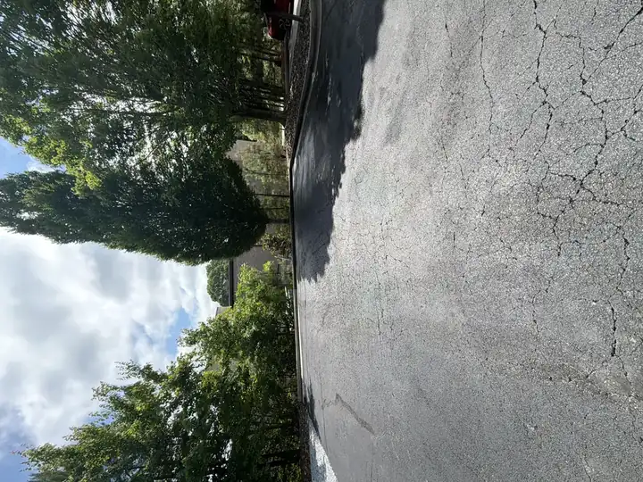 Commercial asphalt parking lot after pressure washing in Alpharetta, GA, showing clean dark pavement and clear access lane under bright partly cloudy sky