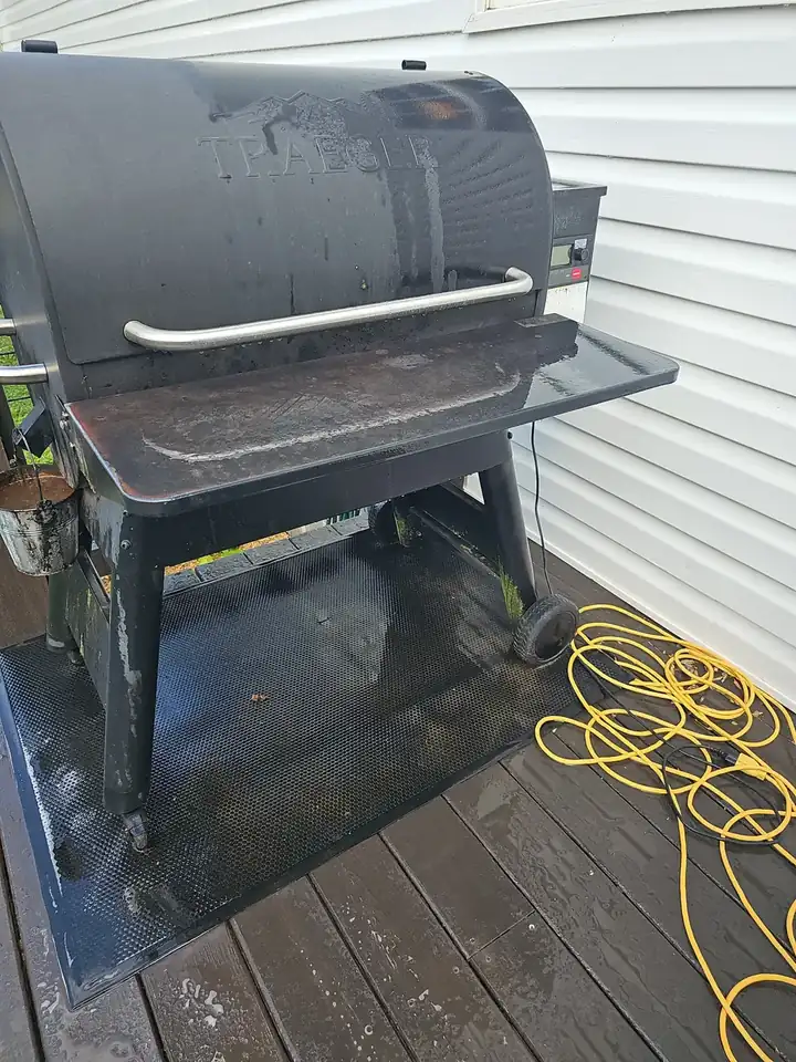 Wet wood deck with a Traeger pellet grill and pressure washing hose visible during a house wash in Canton, GA.