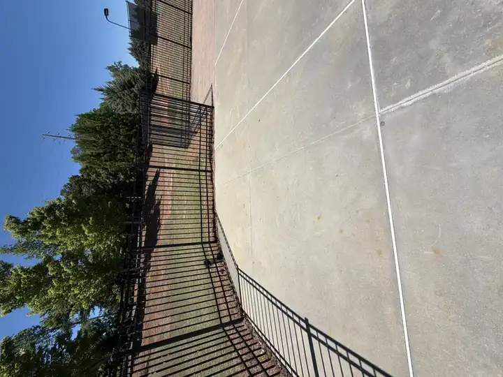 Clean concrete pool deck with iron fence showing rust stains after pressure washing at Canton, GA community pool