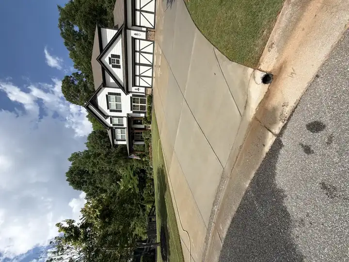 Wide shot of clean concrete driveway after pressure washing in Canton, GA, with three-car garage white farmhouse and blue sky backdrop