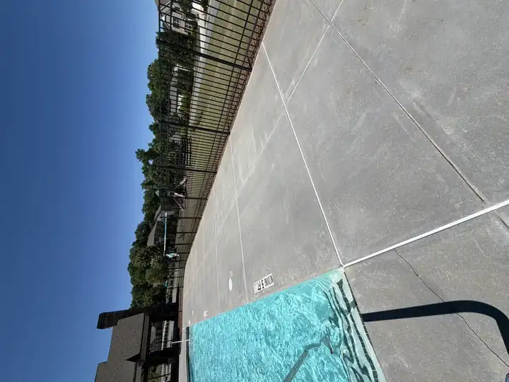 Wide-angle view of pressure-washed concrete pool deck next to bright blue community pool in Canton, GA