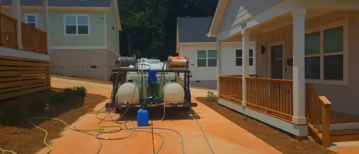 Pressure washing truck and tank setup between new construction homes at a job site in Atlanta, GA, with hoses and chemical tanks staged on concrete.