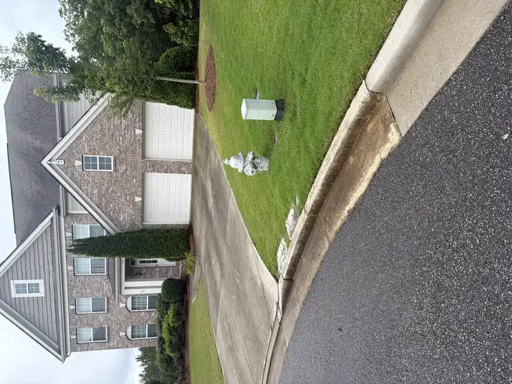 Concrete driveway and curb before pressure washing in Cumming, GA, wide street-level view of two-story brick home