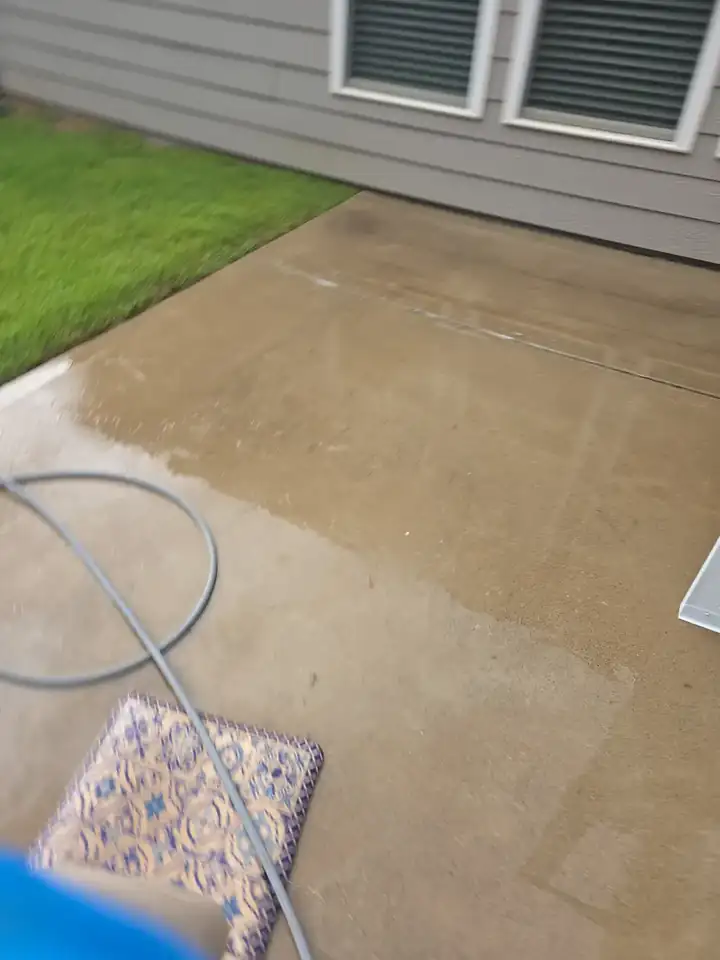 Concrete back patio mid-clean during pressure washing in Woodstock, GA, surface wet with dirt being flushed away