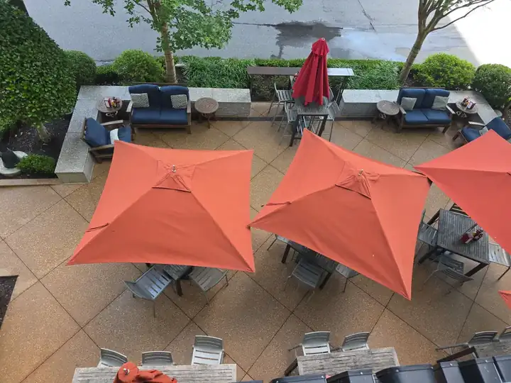 Overhead view of an exposed-aggregate concrete patio with orange umbrellas and seating at a commercial degreasing job in Alpharetta, GA.