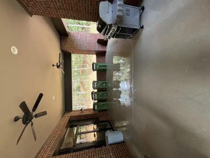 Wet concrete patio floor under a covered brick structure with ceiling fans and a gas grill, during pressure washing in Alpharetta, GA.