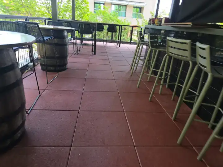 Low-angle view of red concrete tile floor on a covered rooftop patio with barrel tables at a commercial degreasing job in Alpharetta, GA.