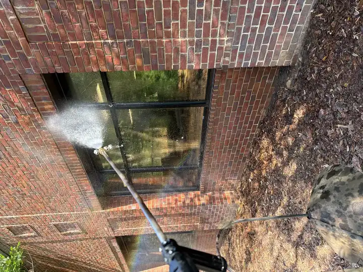 Technician pressure washing commercial building windows on a brick exterior in Alpharetta, GA, with water spraying from an extension wand