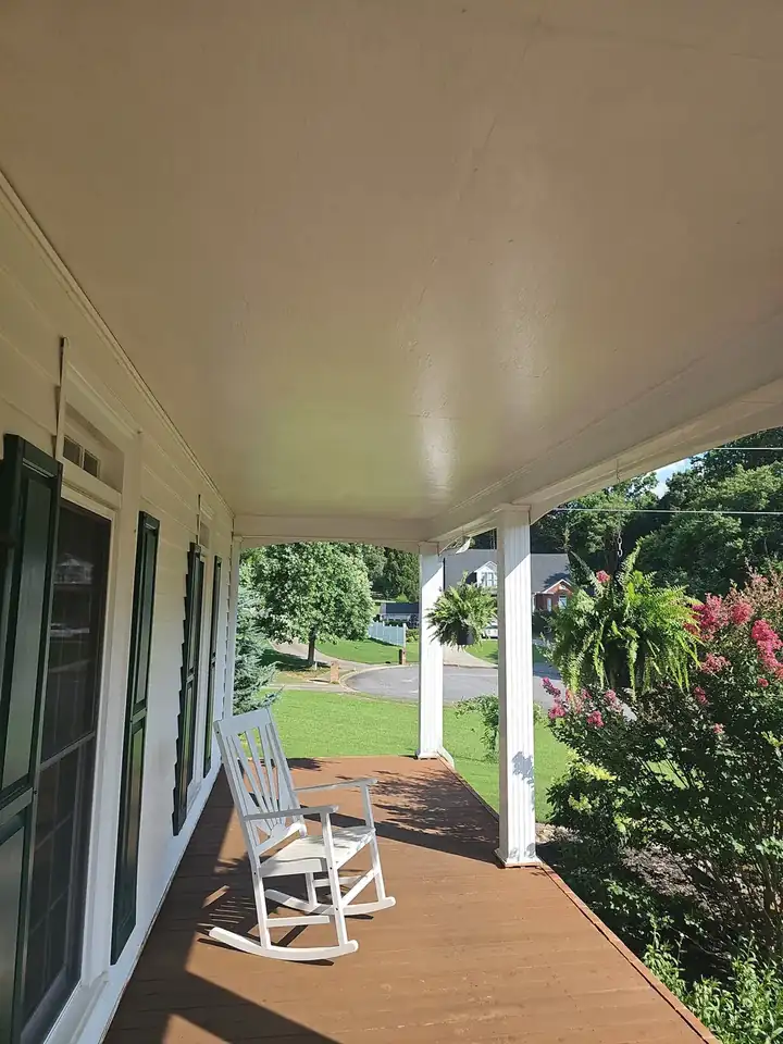 Interior of a covered front porch with wood deck flooring, white columns, and a rocking chair at a Kennesaw, GA home.