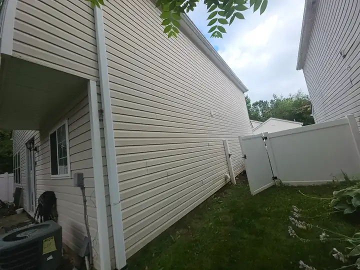Side view of vinyl siding on a two-story home with a white vinyl fence gate visible at a house washing job in Woodstock, GA.