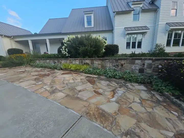 Flagstone courtyard and stone retaining wall beside a white farmhouse at a pressure washing job in Milton, GA.