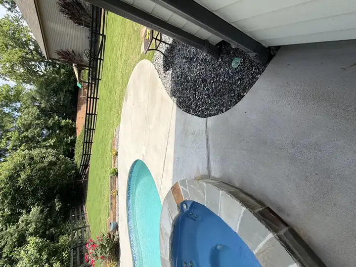 Clean concrete pool and spa deck after pressure washing in Canton, GA, with fenced green lawn and flowering shrubs visible