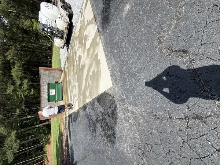 Alpha Pressure Washing technician cleaning a concrete pad near a dumpster enclosure in Alpharetta, GA, with the service trailer visible beside the building