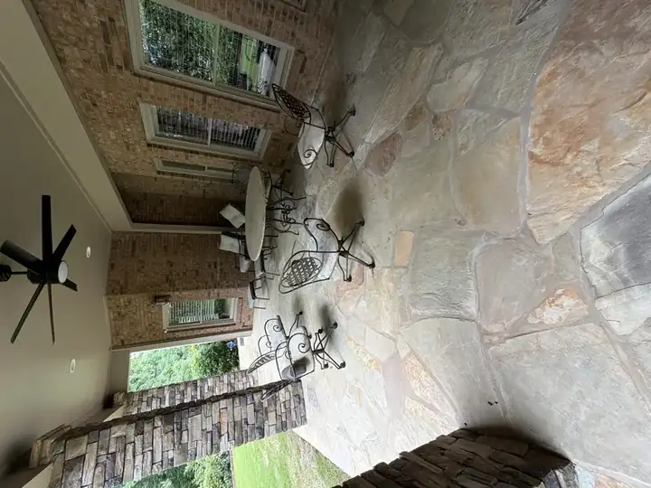 Wide view of a covered flagstone patio with outdoor dining set and stone columns at a Duluth, GA home.