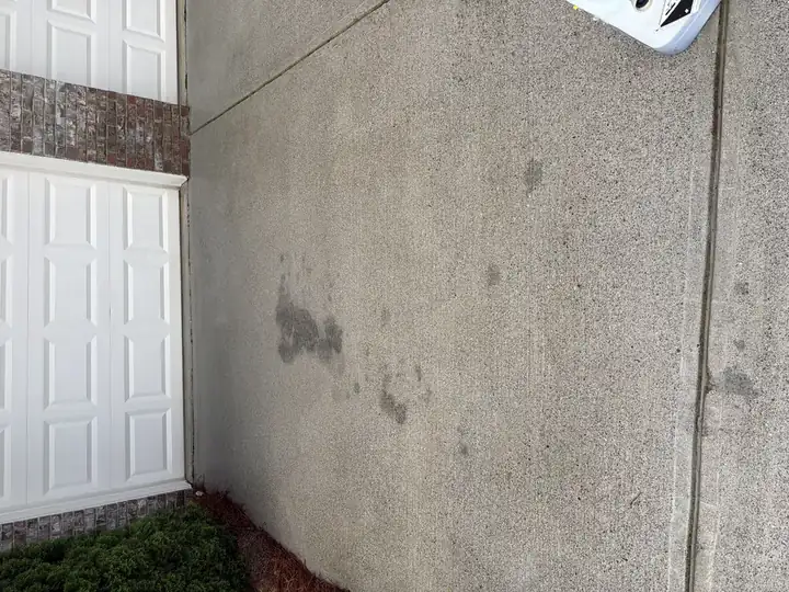Concrete driveway near garage showing heavy oil stains before pressure washing service in Cumming, GA