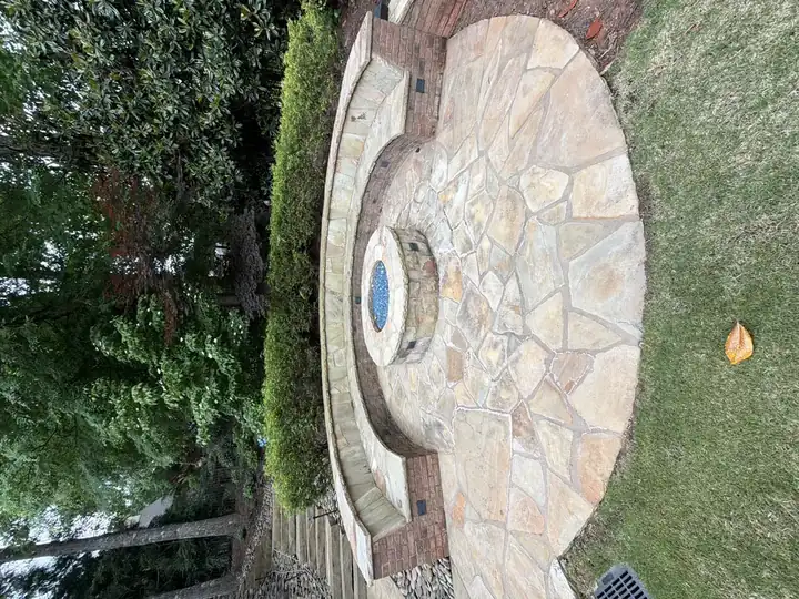 Wide view of a circular flagstone patio with fire pit and curved brick-and-stone seating wall at a residential property in Duluth, GA.