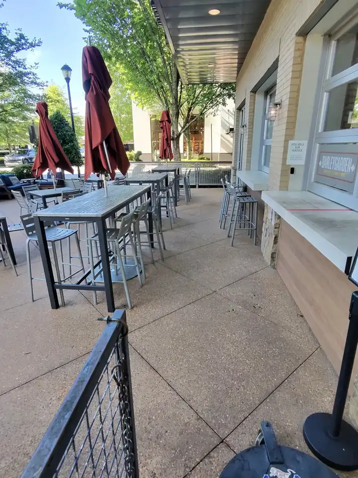 Exposed-aggregate concrete patio and walkway with closed umbrellas and dining tables at a commercial degreasing job in Alpharetta, GA.