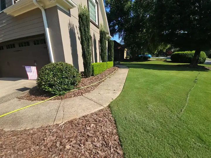 Side concrete walkway along the garage of a residential home in Alpharetta, GA, with pressure washing hose laid out.
