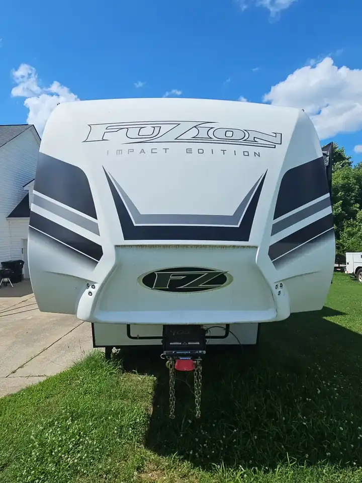 Front nose of a white Fuzion Impact Edition fifth-wheel RV parked on grass at a Canton, GA property.
