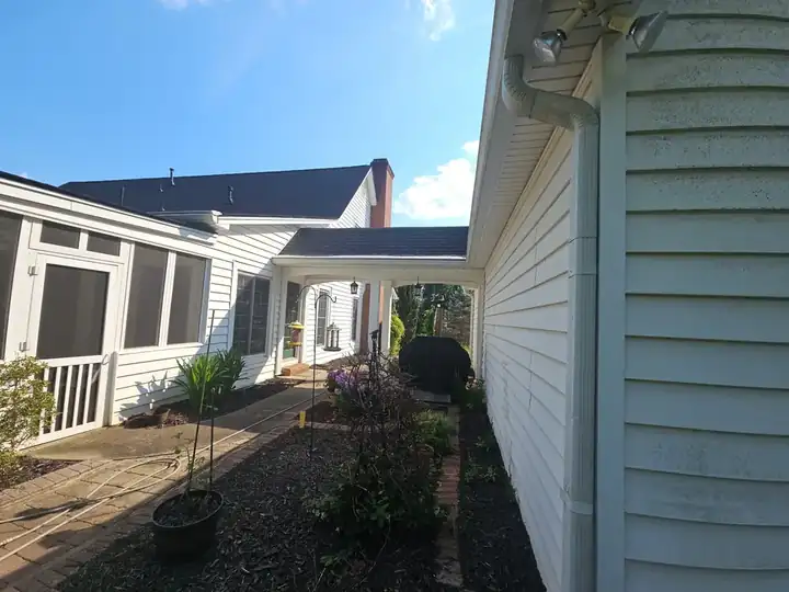 Side of a home showing vinyl siding, a downspout with visible streaking, and the screened porch addition in the background, before a house wash in Kennesaw, GA.