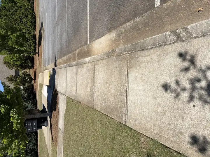 Dirty concrete sidewalk beside a parking lot before pressure washing at a community property in Canton, GA
