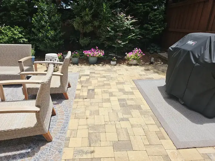 Backyard paver patio with wicker chairs, a covered grill, and flower beds at a residential job in Marietta, GA.