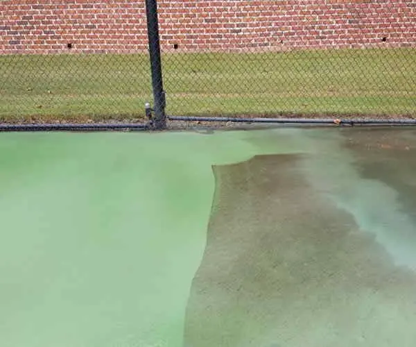 Tennis court surface, darker half beside a lighter cleaned half (Oct 2018)